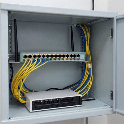 A wall-mounted network cabinet with a router, switch and neatly combed patch cables