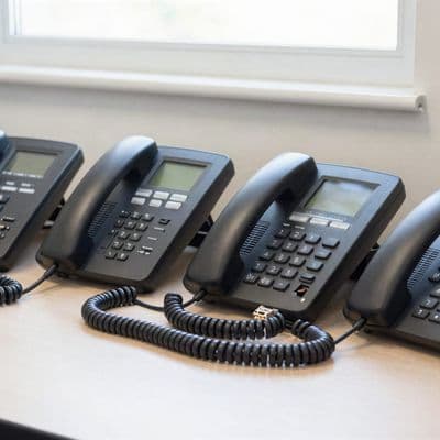 Four desk phones lined up on a table being configured, with coiled network cables beside them