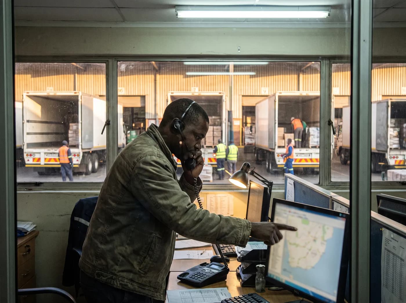 A dispatcher on a desk phone with delivery trucks loading outside