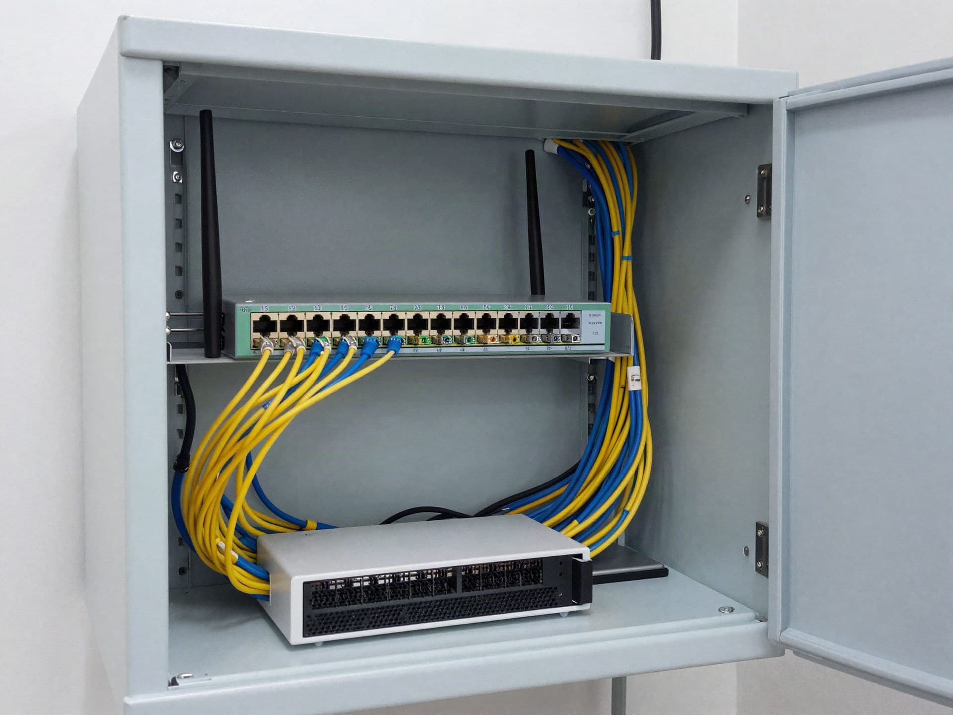 A wall-mounted network cabinet with a router, switch and neatly combed patch cables